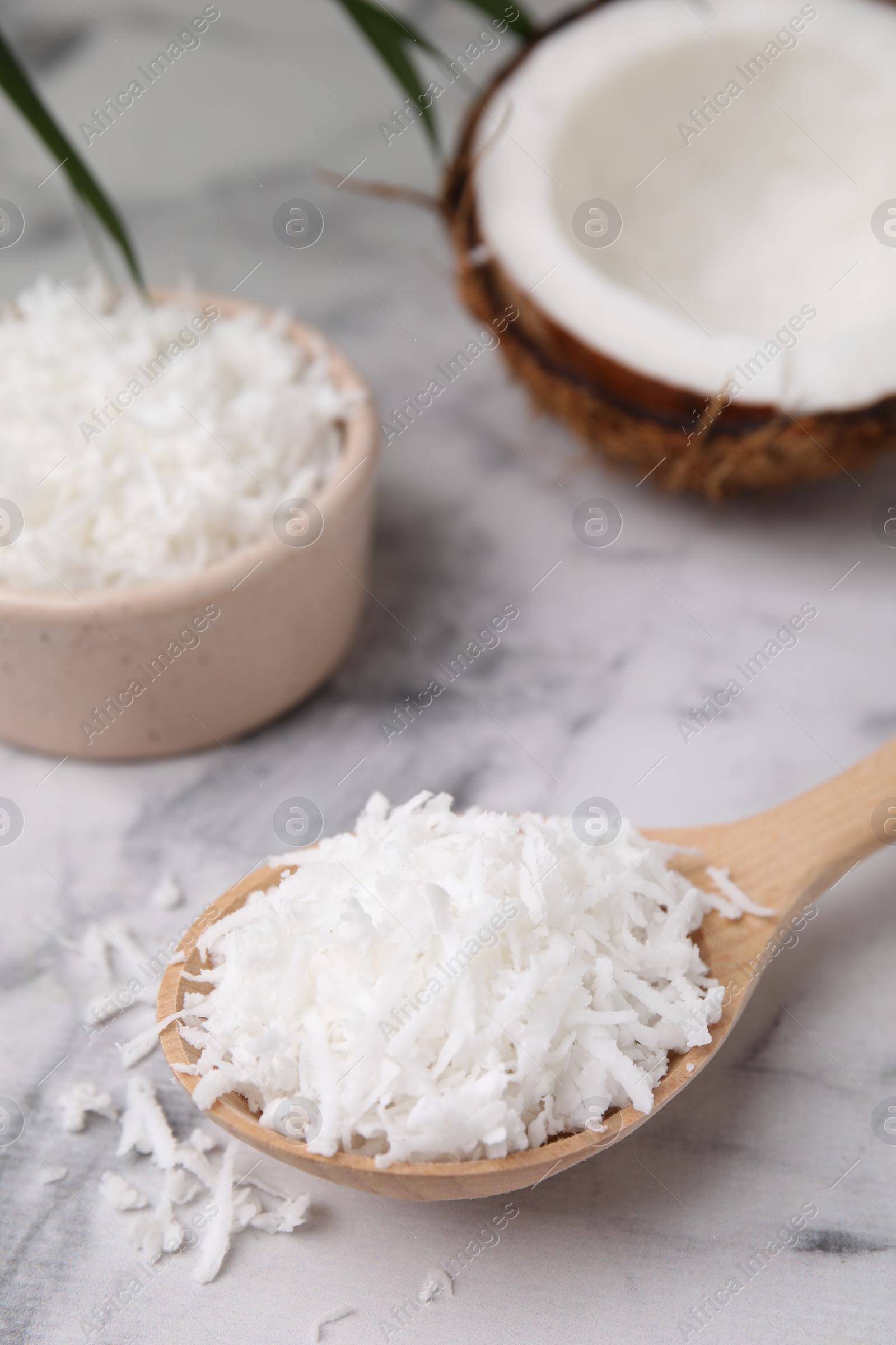 Photo of Coconut flakes in wooden spoon on white marble table