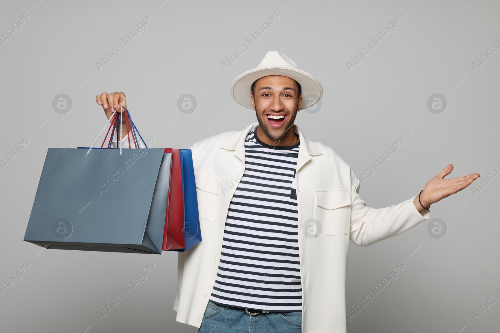 Photo of Happy African American man in hat with shopping bags on light grey background