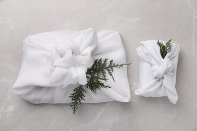 Photo of Furoshiki technique. Gifts packed in white fabric and thuja branches on grey marble table, flat lay