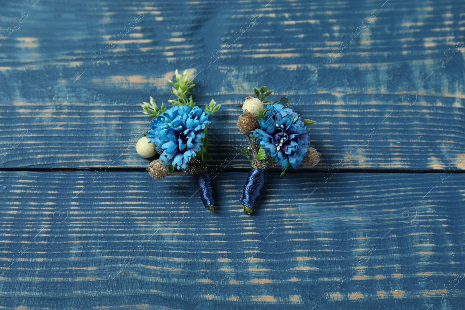 Photo of Stylish boutonnieres on blue wooden table, top view