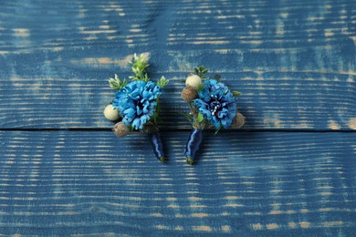 Stylish boutonnieres on blue wooden table, top view