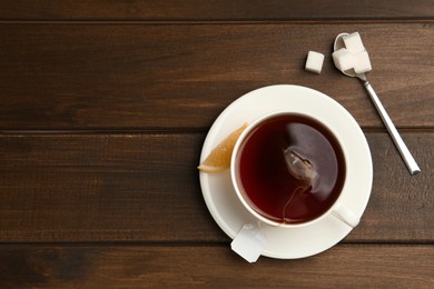 Photo of Tea bag in ceramic cup of hot water and sugar on wooden table, flat lay. Space for text