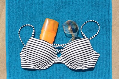 Blue beach towel, sunglasses, sunscreen and swimsuit on sand, flat lay