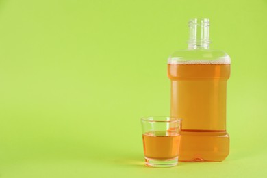Photo of Bottle and glass with mouthwash on light green background, space for text