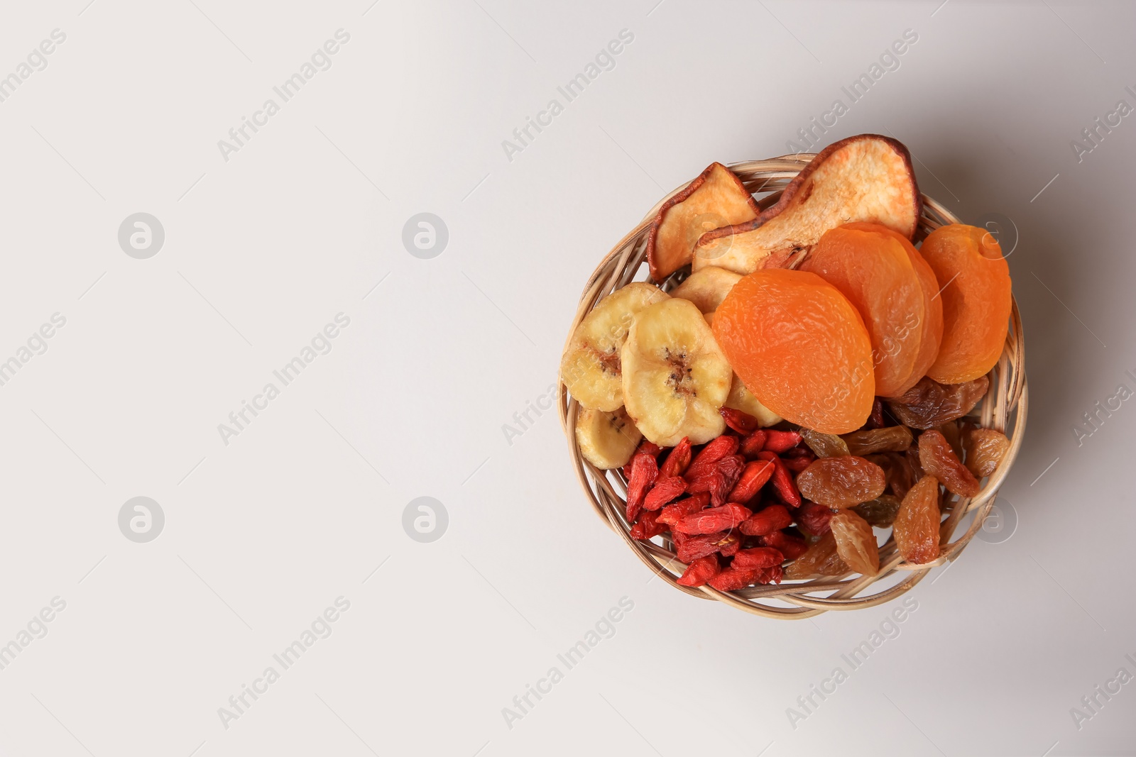 Photo of Wicker basket with different dried fruits on white background, top view. Space for text