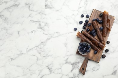 Photo of Delicious fruit leather rolls and blueberries on white marble table, flat lay. Space for text