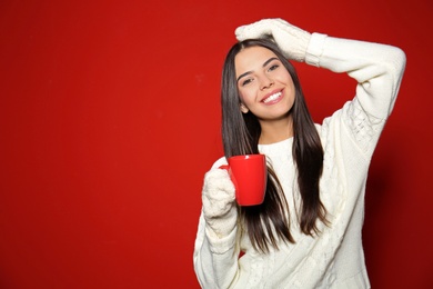 Photo of Young woman in warm sweater with cup of hot drink on red background. Space for text
