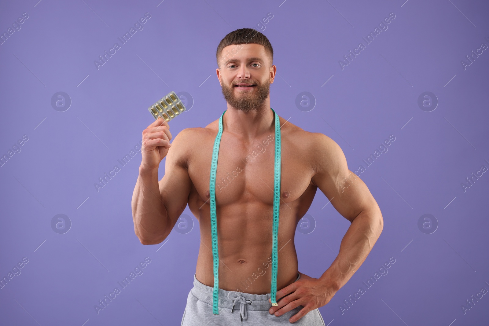 Photo of Athletic young man with measuring tape and pills on purple background. Weight loss