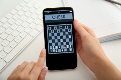 Image of Woman playing online chess on smartphone at table, closeup