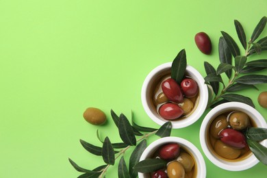 Photo of Bowls with different ripe olives and leaves on light green background, flat lay. Space for text