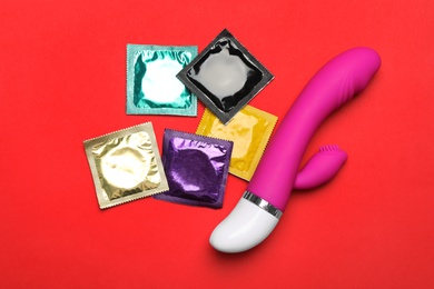 Vibrator and condoms on red background, top view. Sex game