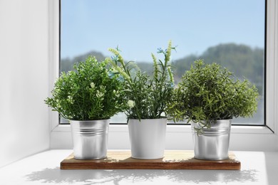 Photo of Artificial potted herbs on sunny day on windowsill indoors. Home decor