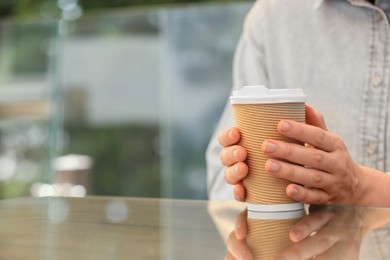 Woman holding takeaway paper cup at table, closeup and space for text. Coffee to go