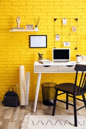 Stylish home office interior with comfortable workplace near yellow brick wall