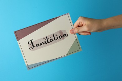 Woman holding beautiful card with word Invitation on light blue background, closeup