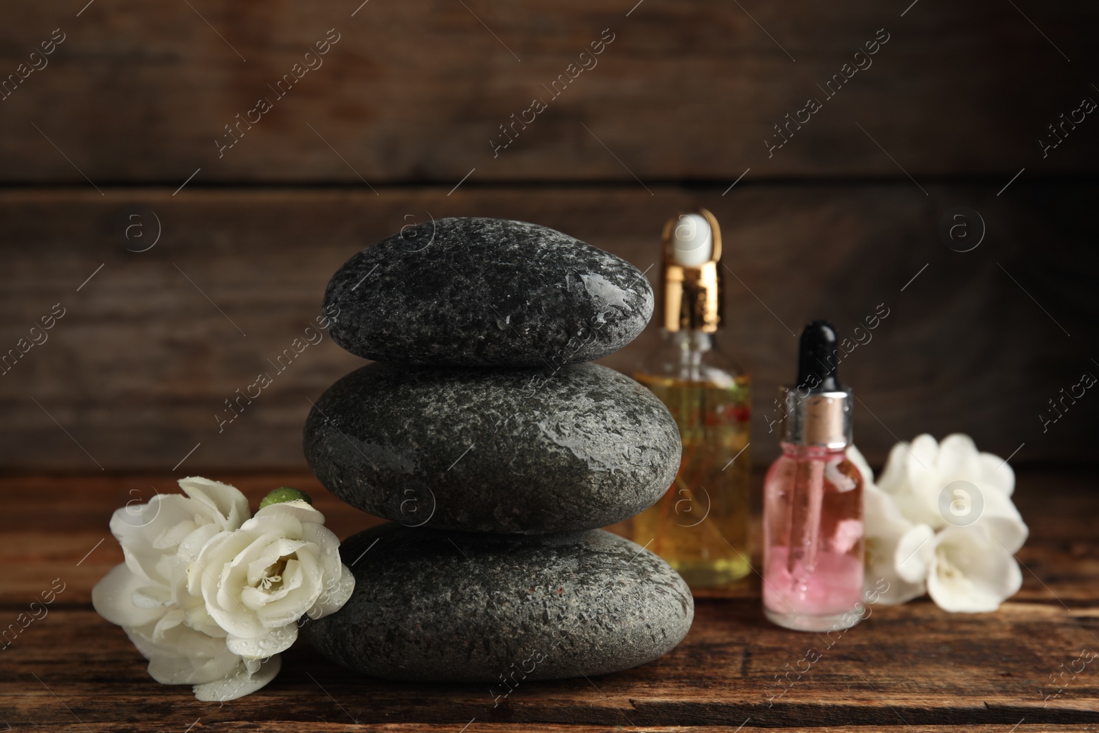 Photo of Stack of grey spa stones, flowers and oils on wooden table