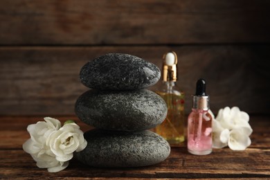 Photo of Stack of grey spa stones, flowers and oils on wooden table
