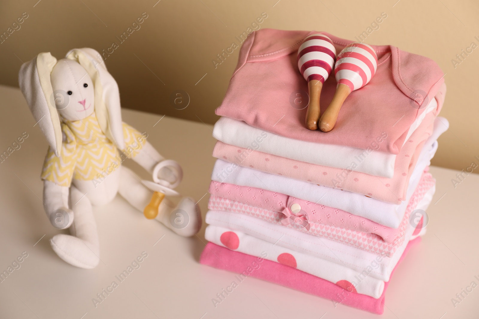 Photo of Stack of baby girl's clothes, rattles, pacifier and toy bunny on white table