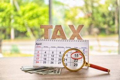 Word TAX, calendar, magnifier and money on table