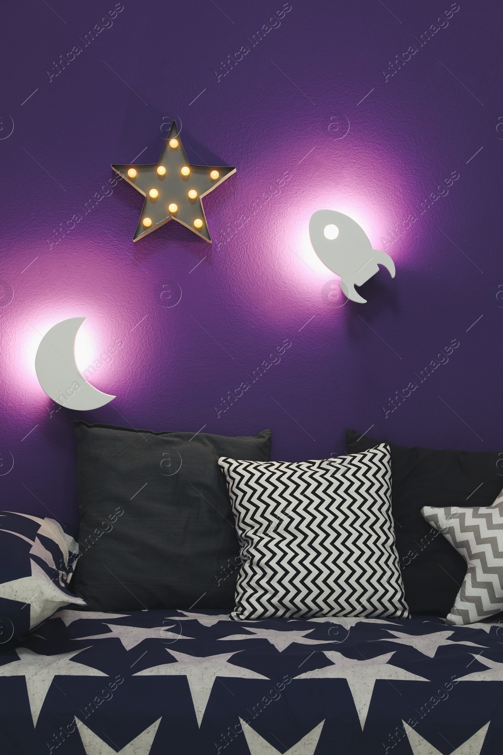 Photo of Room interior with bed and different night lamps on purple wall