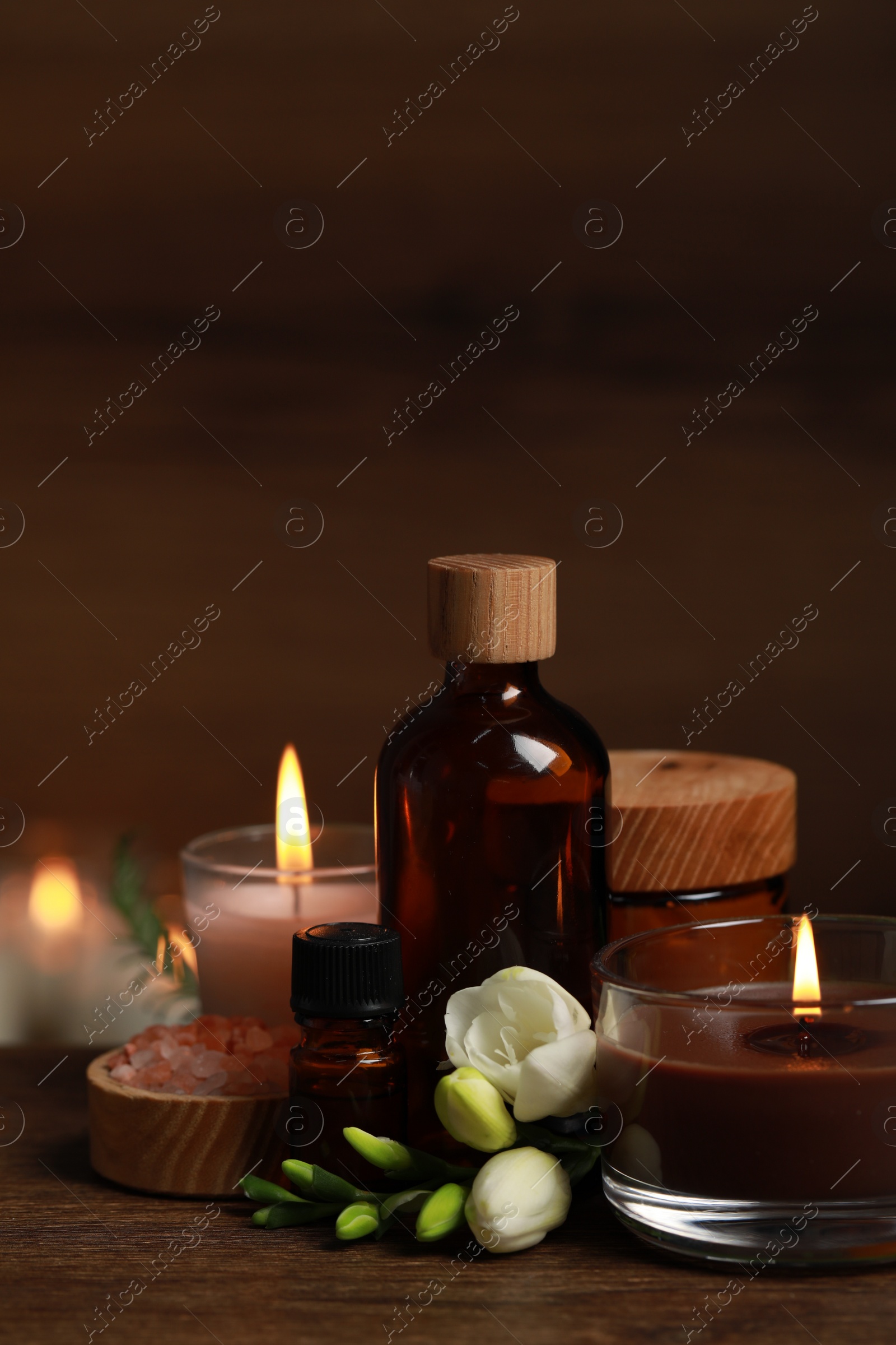 Photo of Beautiful spa composition with burning candles, different care products and flowers on wooden table