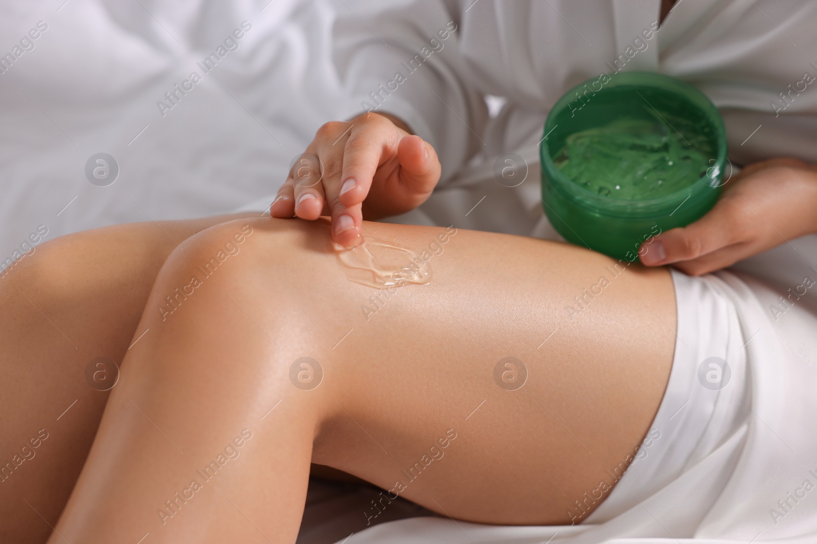 Photo of Young woman applying aloe gel onto her leg on bed, closeup