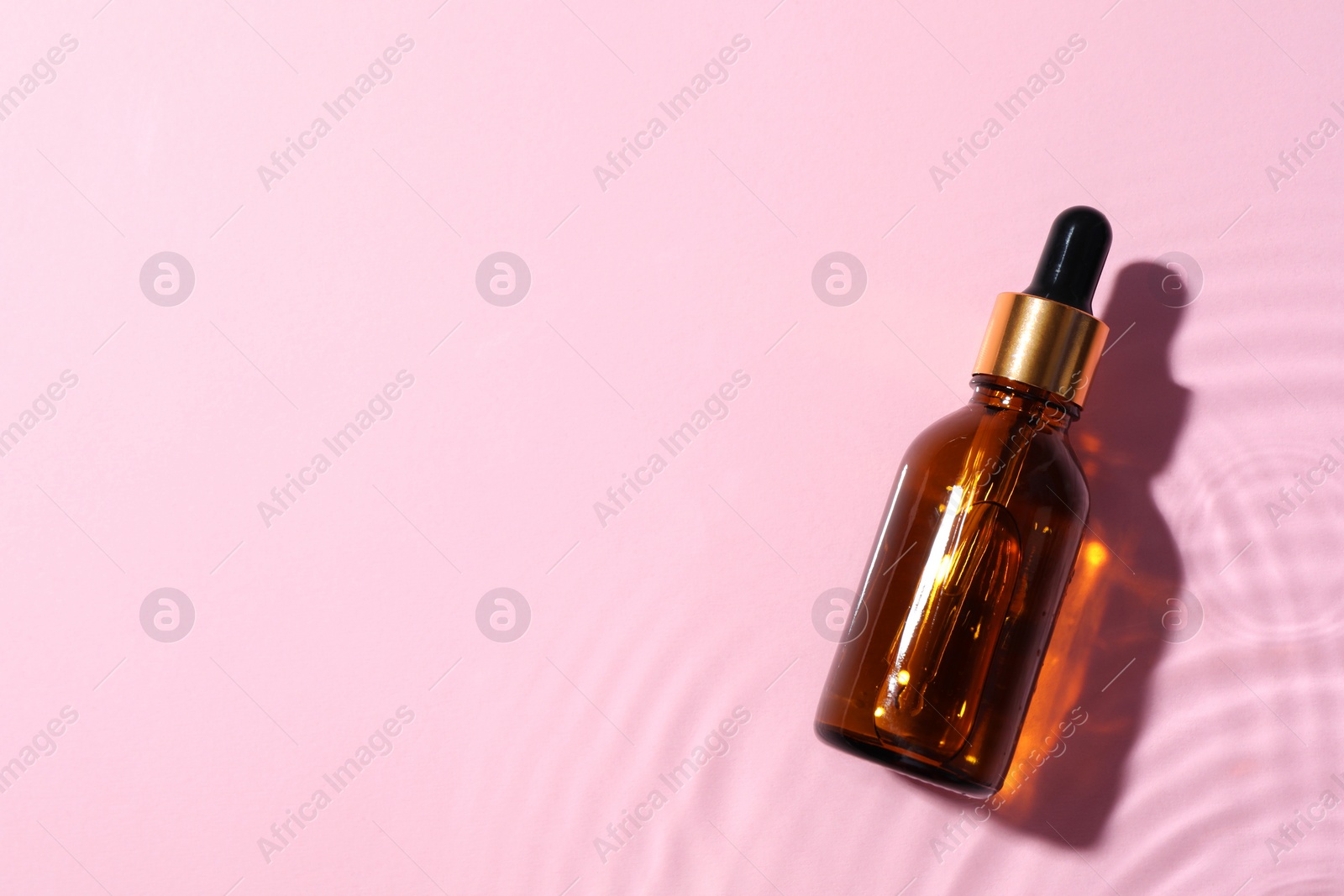 Photo of Bottle of cosmetic oil in water on pink background, top view. Space for text