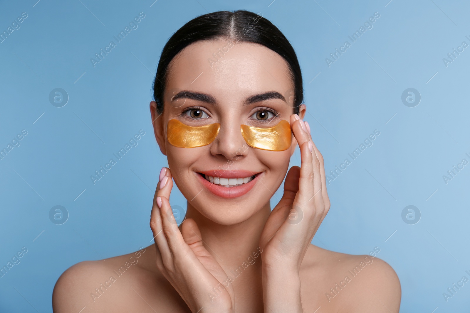 Photo of Beautiful young woman with under eye patches on light blue background