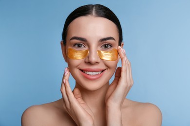 Photo of Beautiful young woman with under eye patches on light blue background