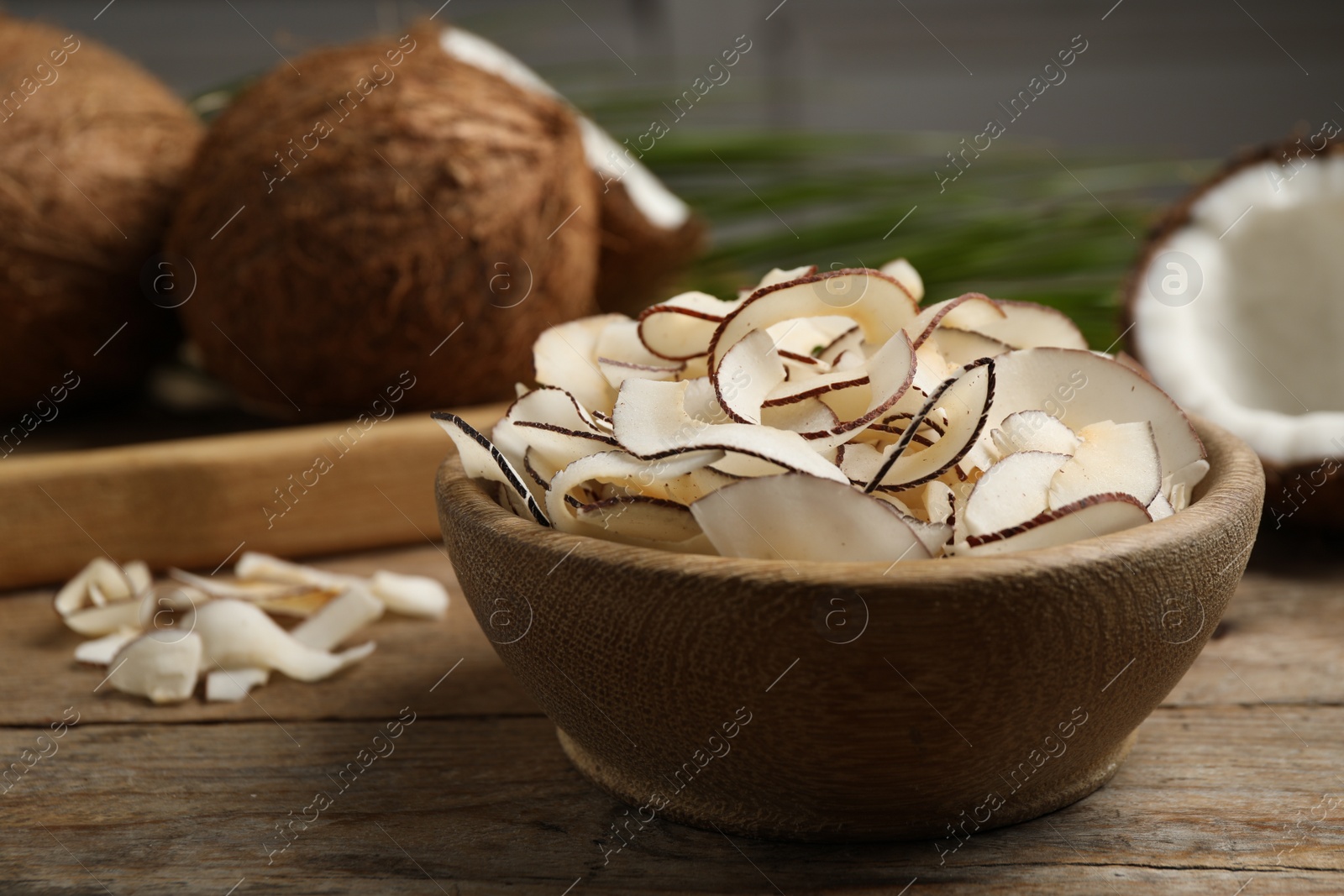 Photo of Tasty coconut chips in bowl on wooden table