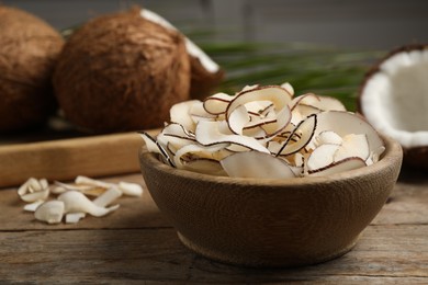 Tasty coconut chips in bowl on wooden table