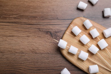 Photo of Sticks with delicious puffy marshmallows on wooden table, flat lay. Space for text