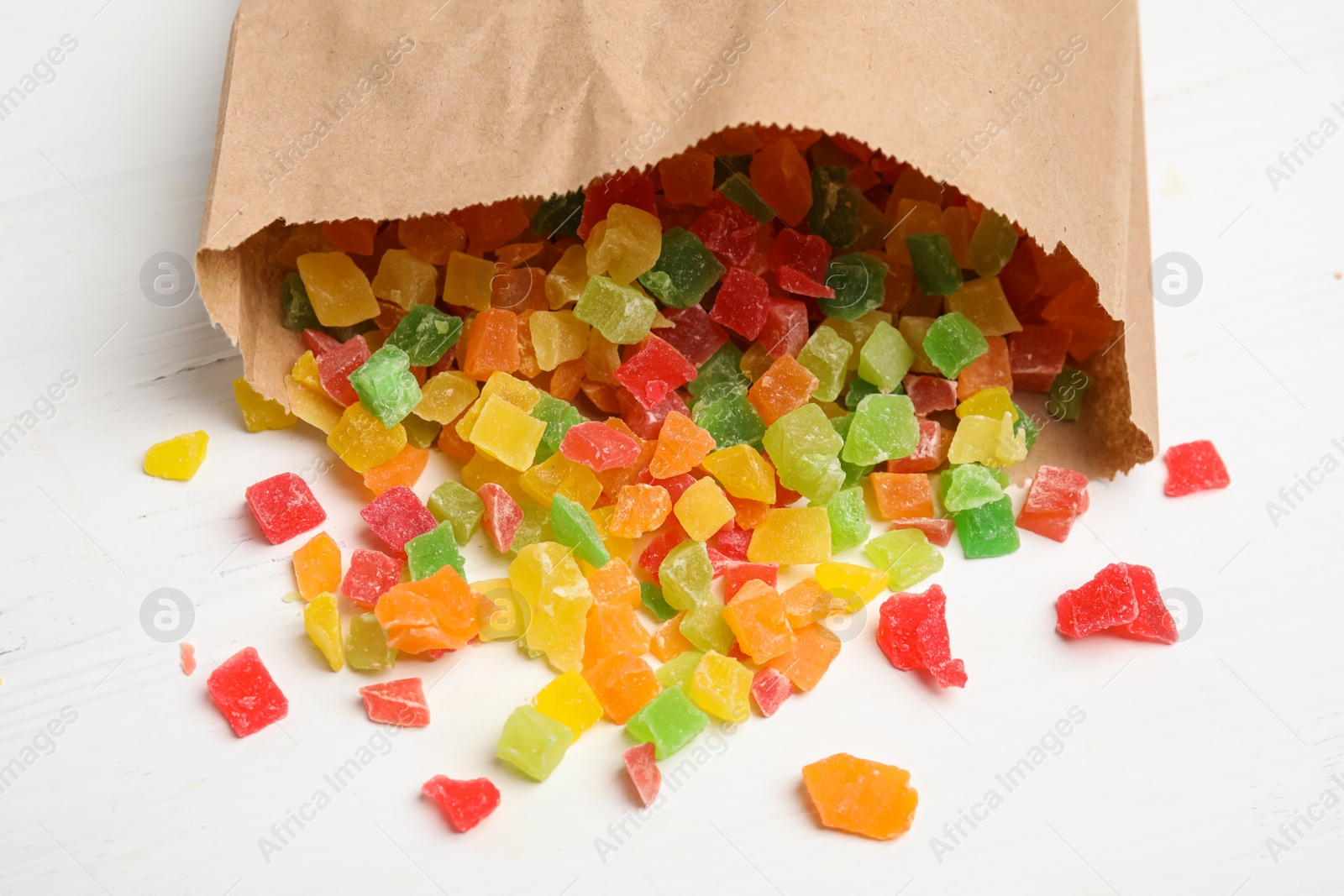 Photo of Overturned paper bag with mix of delicious candied fruits on white wooden table, closeup