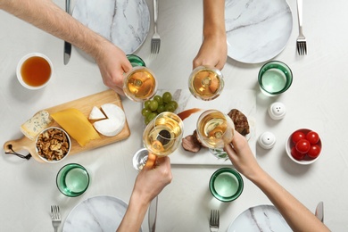 Photo of People holding glasses of white wine over table with tasty snacks, top view