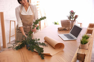 Photo of Florist making beautiful bouquet at table in workshop, closeup