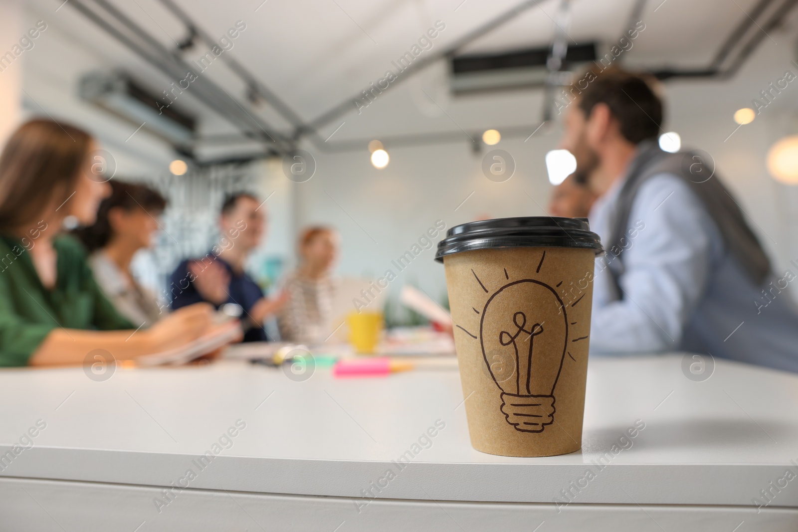 Photo of Team of employees working together in office. Paper cup of drink on white table, selective focus