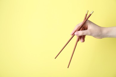 Woman holding pair of wooden chopsticks on yellow background, closeup. Space for text