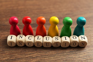 Colorful pawns and cubes with word Inclusion on wooden table, closeup