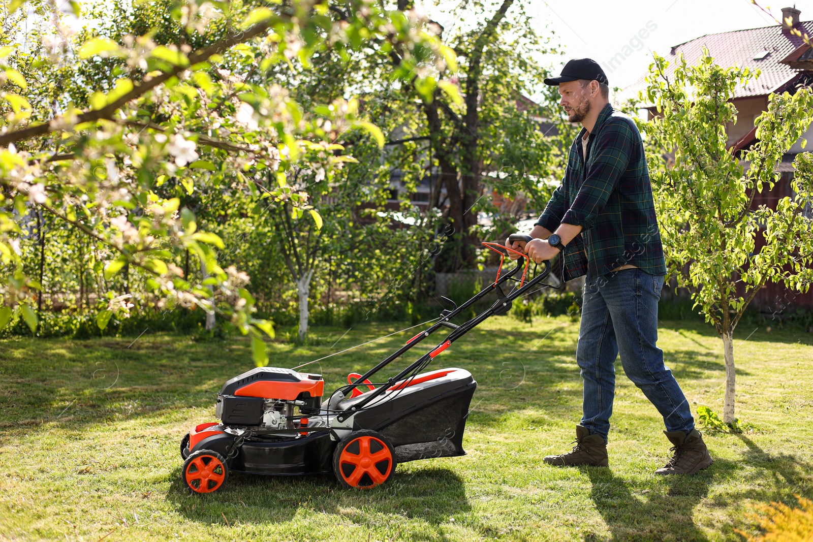 Photo of Man cutting green grass with lawn mower in garden