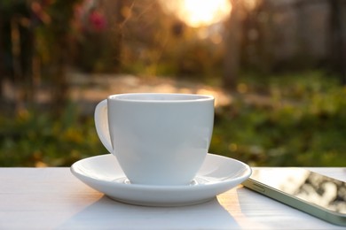 Photo of White cup with coffee on wooden table in morning outdoors