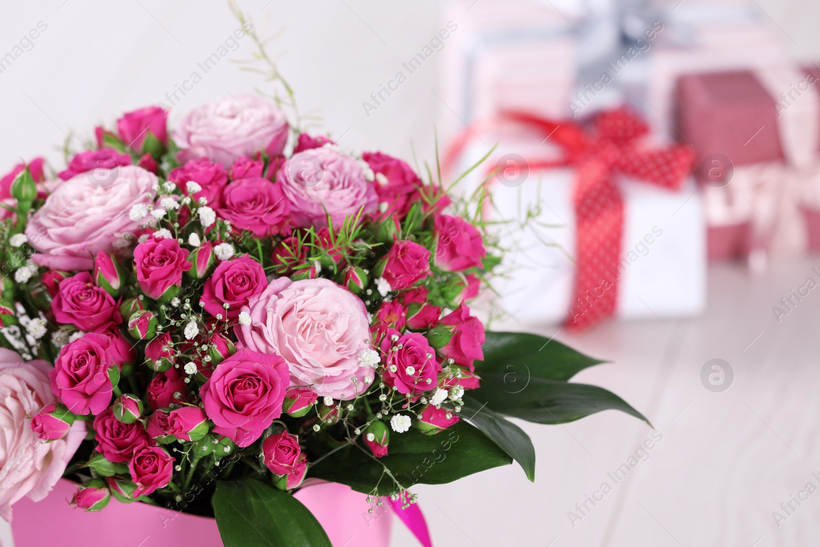 Photo of Beautiful bouquet of flowers and blurred gifts on background. Space for text