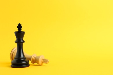 Photo of Black king near fallen white one on yellow background, space for text. Game of chess