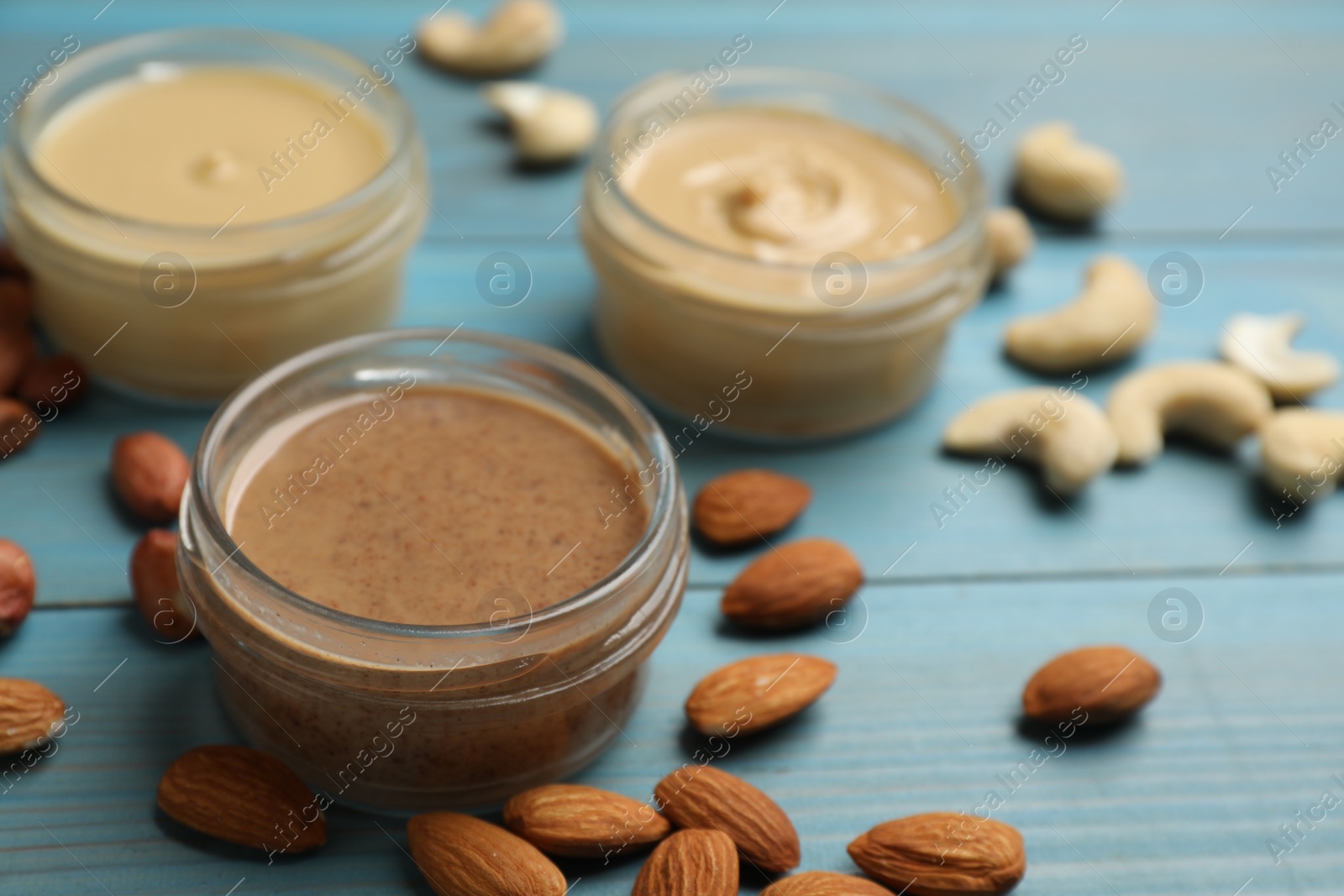 Photo of Jars with butters made of different nuts and ingredients on light blue wooden table, closeup. Space for text