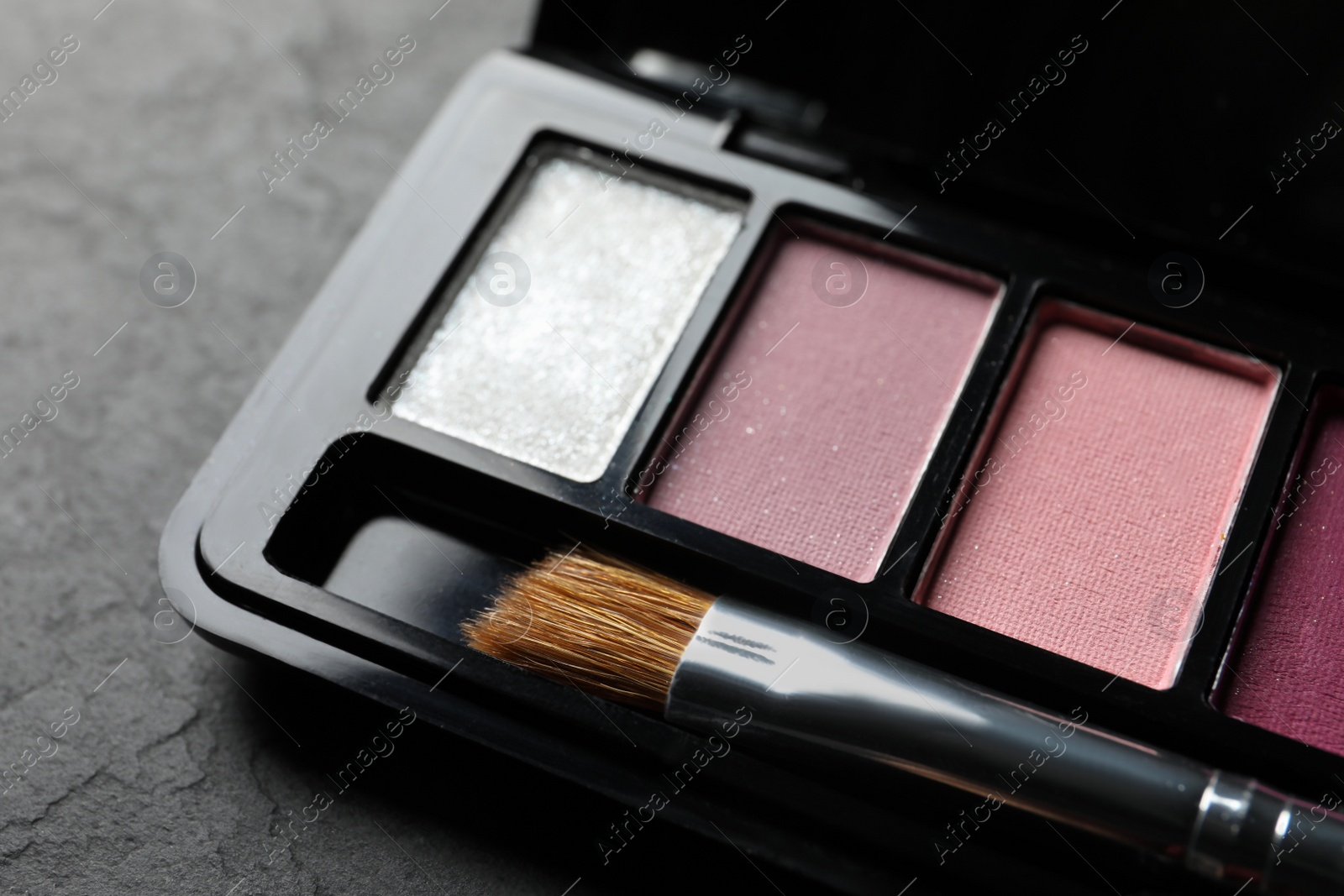Photo of Beautiful eye shadow palette with brush on dark grey textured table, closeup