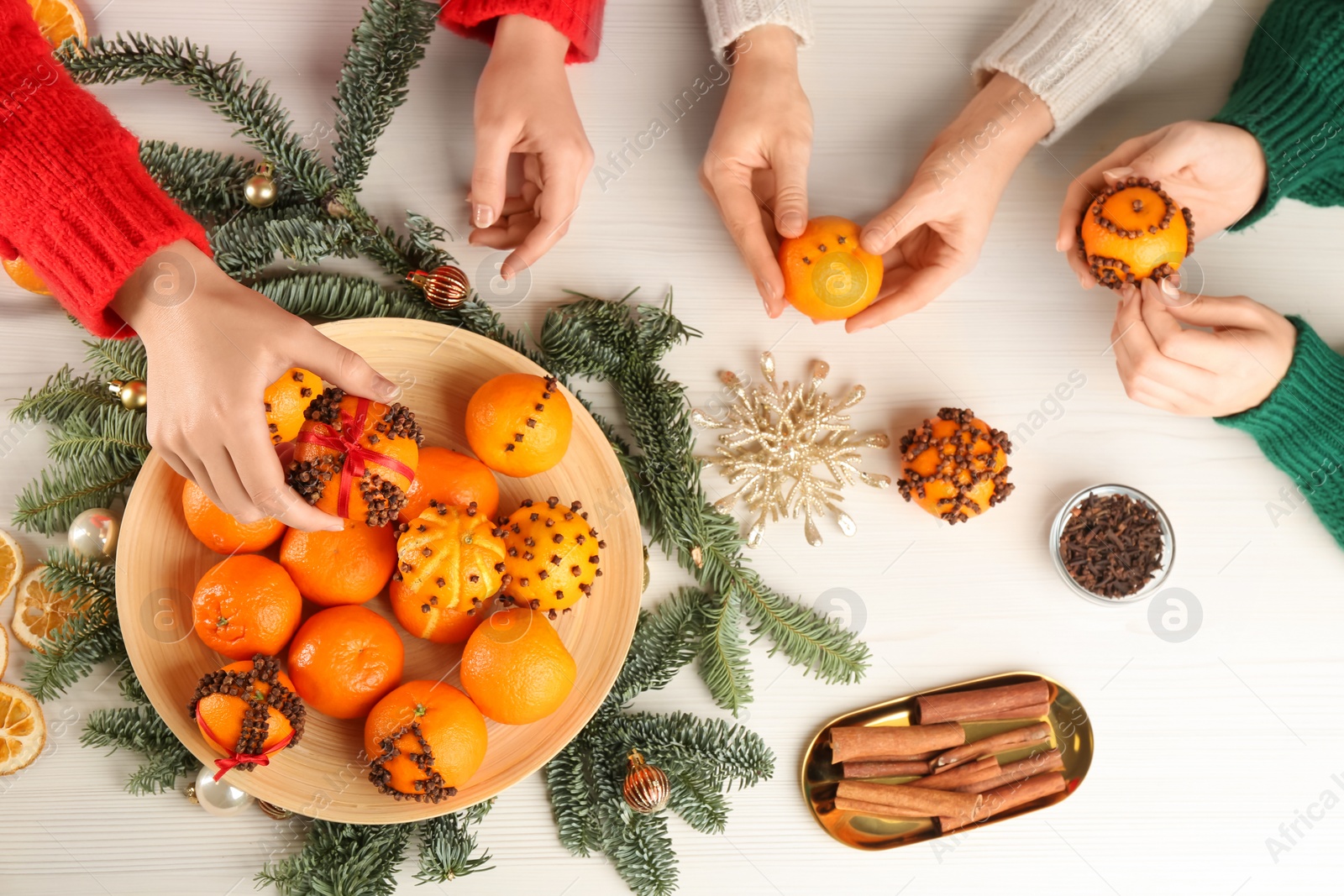 Photo of Friends decorating fresh tangerines with cloves at light table, top view. Making Christmas pomander balls