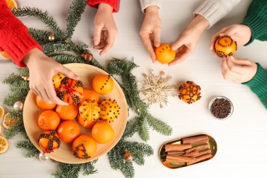 Friends decorating fresh tangerines with cloves at light table, top view. Making Christmas pomander balls