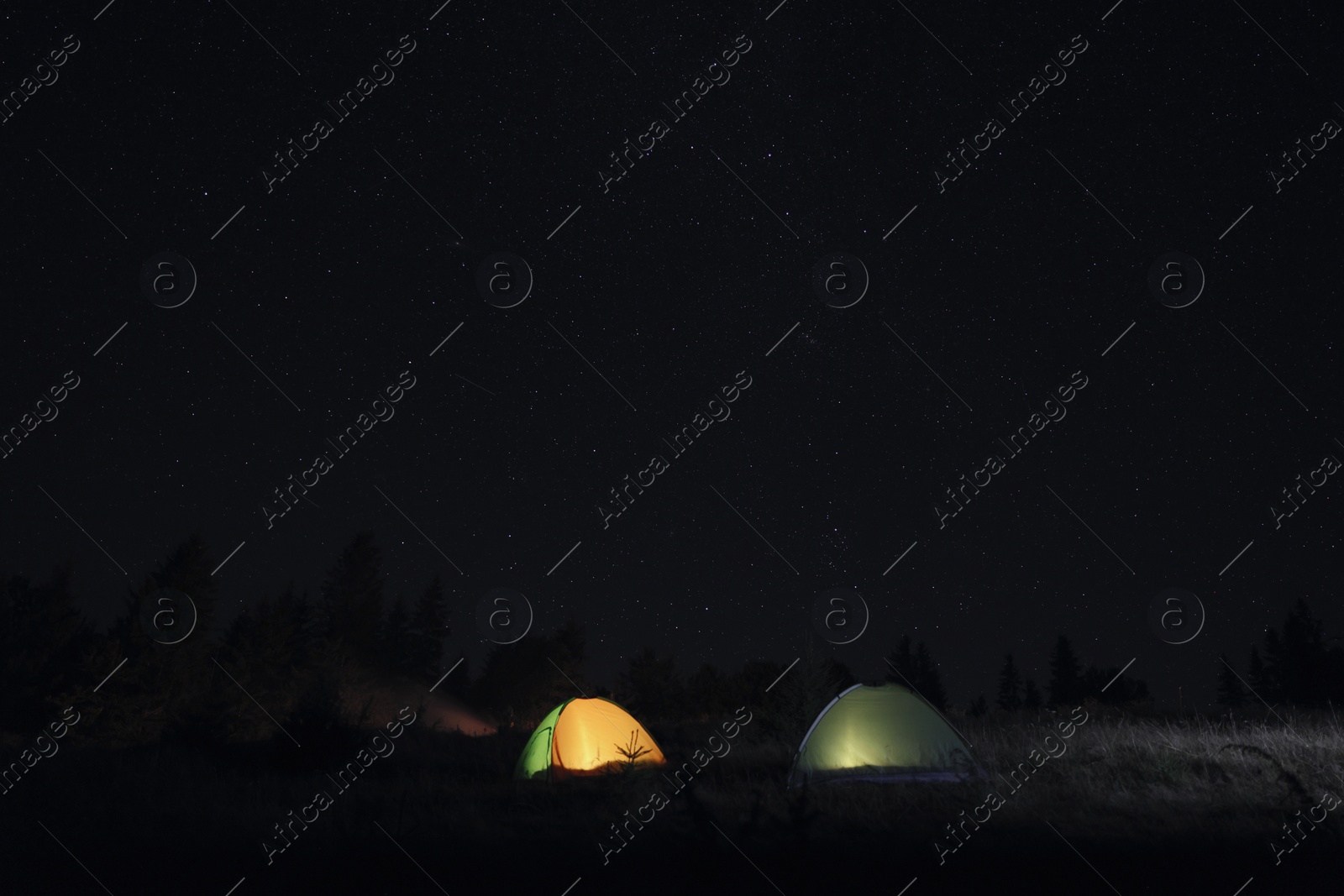 Photo of Two color camping tents near forest under sky full of stars at night