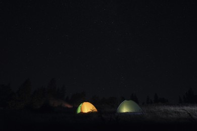 Photo of Two color camping tents near forest under sky full of stars at night