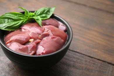 Photo of Bowl of raw chicken liver with basil on wooden table, closeup. Space for text
