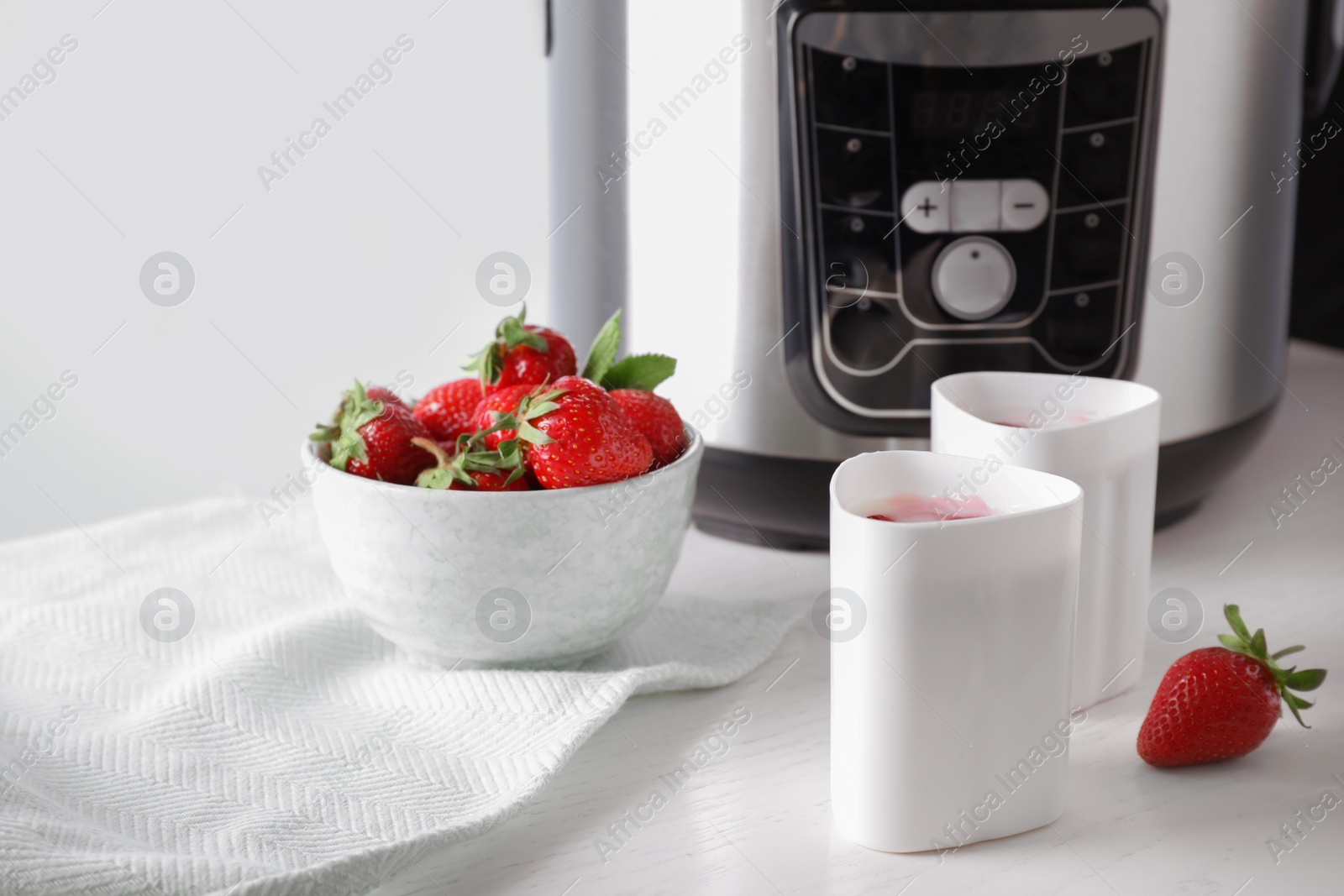 Photo of Cups of homemade yogurt, strawberries and multi cooker on table